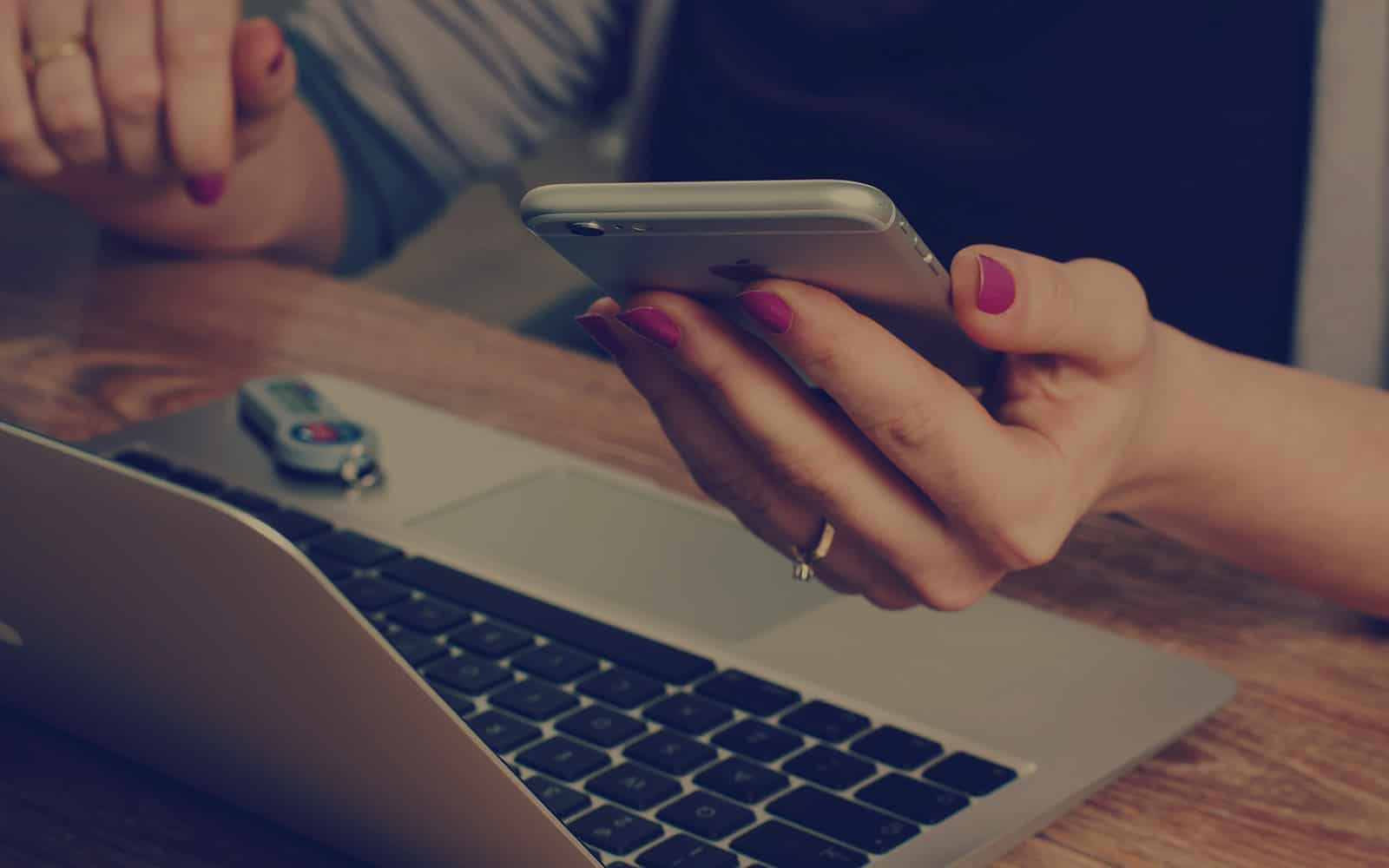 en person, der bruger en mobiltelefon ved siden af en bærbar computer.
