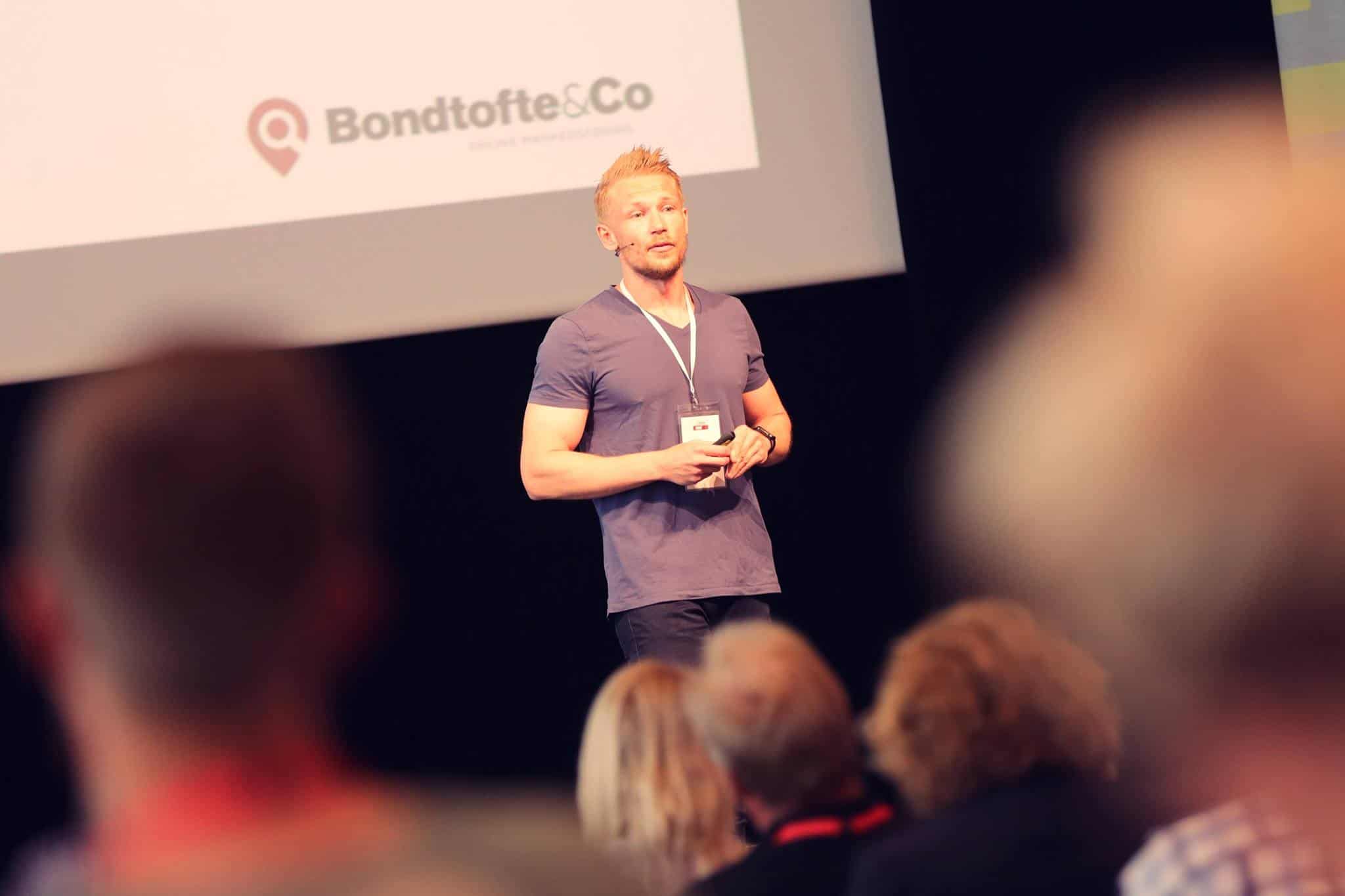 henrik-bondtofte | Henrik Bondtofte en mand, der står på en scene foran en menneskemængde.